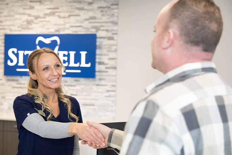 satff member shaking hands with patient at the front desk within the dental practice