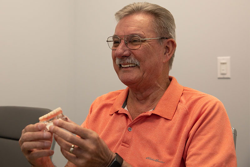 Patient smiling while holding implant model within the dental practice