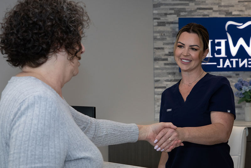 patient and staff member shaking hands at the front desk within the dental practice